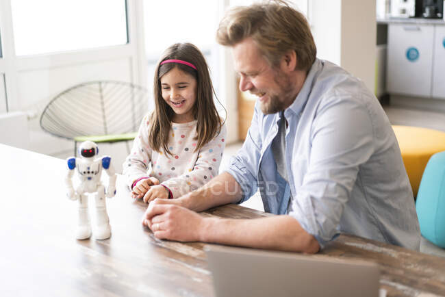 Sorridente padre e figlia guardando robot giocattolo sul tavolo — Foto stock