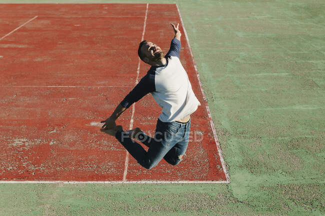 Hombre feliz saltando en la cancha deportiva durante el día soleado - foto de stock
