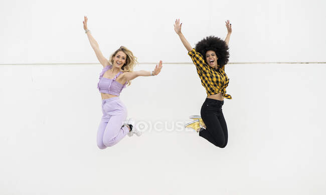 Весёлые подруги прыгают через стену на улице — стоковое фото