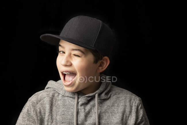 Mischievous garçon clin d'oeil en face de fond noir — Photo de stock