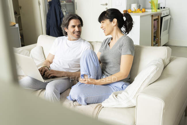 Man with laptop discussing with woman while sitting on sofa in living room at home — Stock Photo