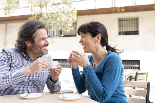 Щаслива зріла пара посміхається, маючи каву на терасі — стокове фото