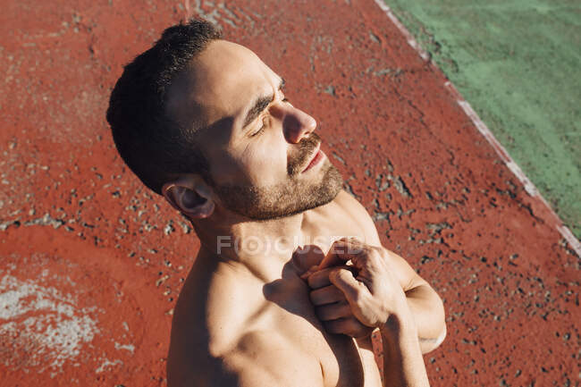 Shirtless man with hand on chest standing on sports court during sunny day — Stock Photo