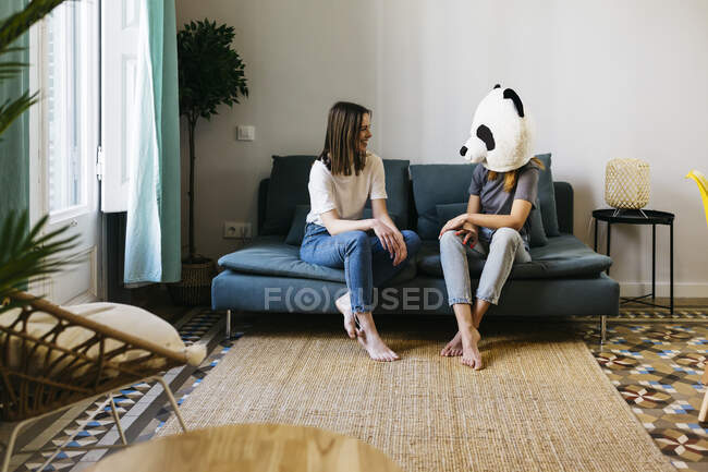 Sorrindo mulher olhando para namorada vestindo máscara de panda na sala de estar — Fotografia de Stock