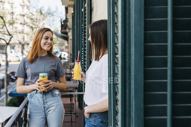 Sorridente donna godendo di succo di frutta con la fidanzata mentre in piedi sul balcone — Foto stock