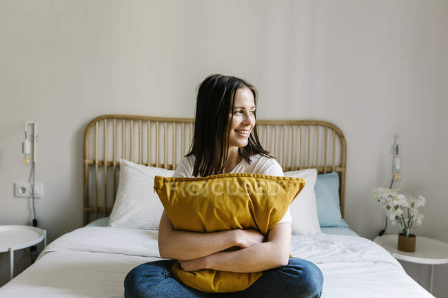 Lächelnde Frau umarmt Kissen auf dem Bett zu Hause — Stockfoto
