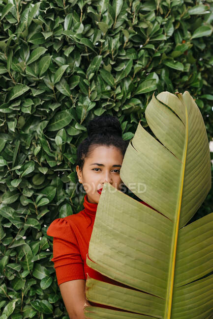 Frau blickt durch Bananenblatt, während sie vor grünen Pflanzen steht — Stockfoto