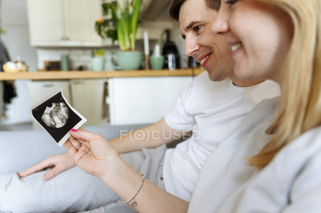Smiling husband and wife looking at ultrasound picture at home — Stock Photo