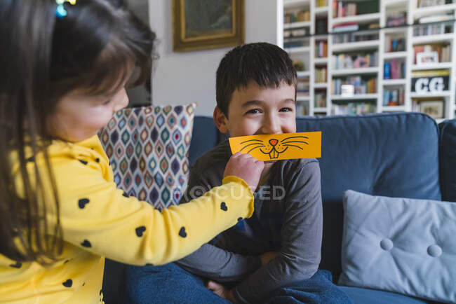 Niño y niña jugando con emoticono animal en casa - foto de stock
