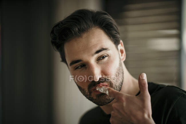 Hombre guapo mirando hacia otro lado mientras lame el dedo - foto de stock