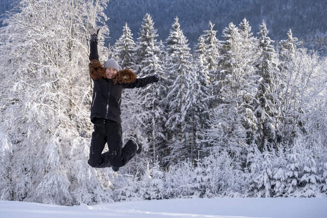 Mujer despreocupada con los ojos cerrados saltando sobre la nieve durante el invierno - foto de stock