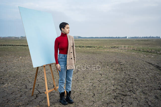 Mujer contemplando mientras está de pie pintando en el campo agrícola - foto de stock