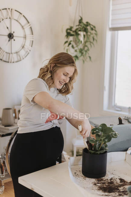 Mujer feliz poniendo tierra en maceta planta en casa - foto de stock