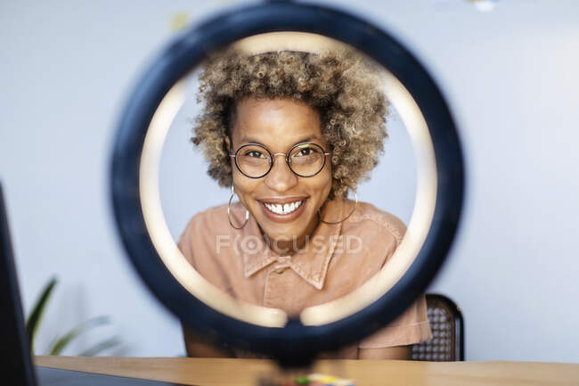 Influenceur féminin avec des lunettes regardant à travers la lumière anneau au bureau à la maison — Photo de stock