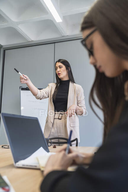 Mujer de negocios señalando mientras una colega escribe durante la reunión en la oficina - foto de stock
