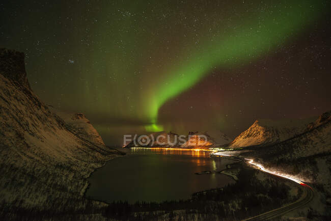 Norway, Tromso, Bergsbotn, Scenic view of Aurora Borealis over illuminated fjord village on Senja Island — Stock Photo