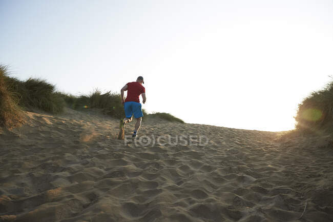 Sportsperson exercising while running on sand dune at sunrise — Stock Photo