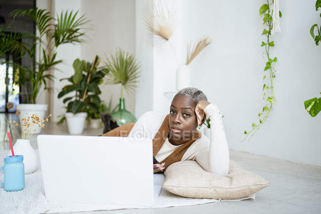 Femme entrepreneur avec la tête à la main couchée sur le sol devant un ordinateur portable à la maison — Photo de stock