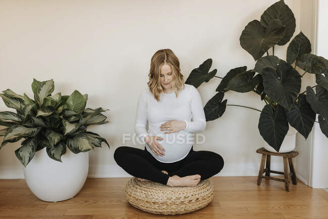 Giovane donna con le mani sullo stomaco seduta croce gambe a casa — Foto stock
