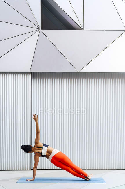 Средняя взрослая спортсменка, практикующая боковую доску на тренажерном коврике — стоковое фото