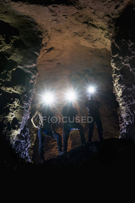 Turistas masculinos con faros iluminados de pie en la cueva - foto de stock
