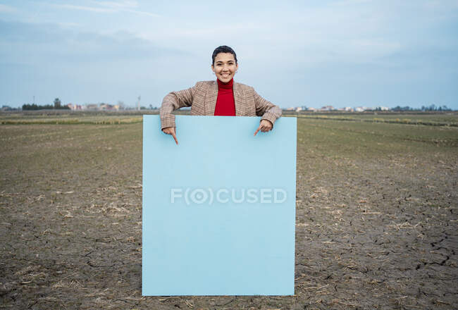 Mujer sonriente señalando la pintura azul en el campo - foto de stock