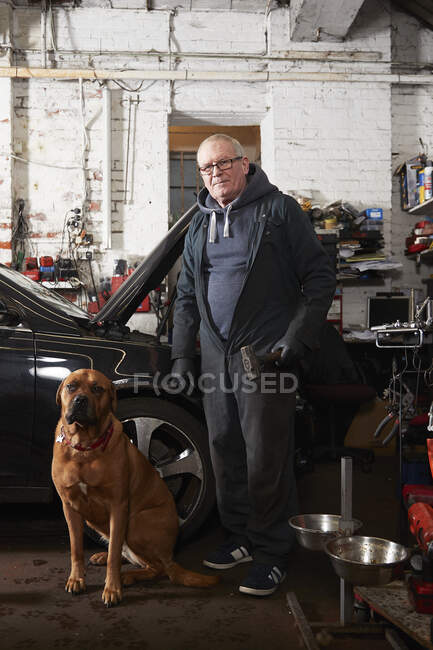 Automechaniker mit Hund steht in Werkstatt — Stockfoto
