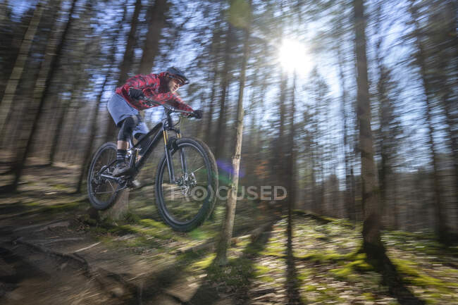 Male athlete in mid-air with mountain bike in forest — Stock Photo