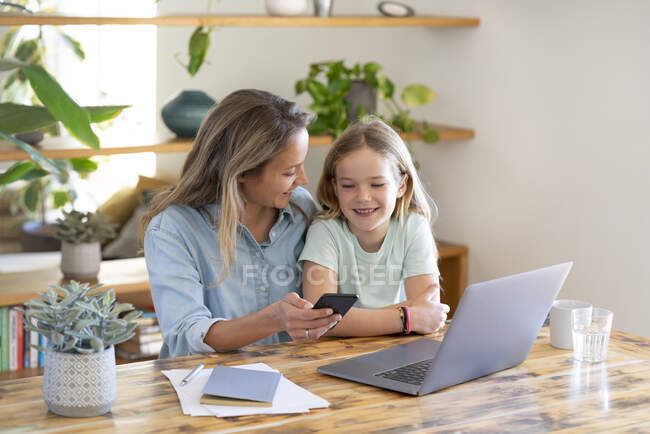 Бизнесмен и дочь сидят за столом с ноутбуком и смартфоном — стоковое фото