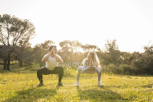 Giovani amici accovacciati mentre si esercitano insieme nella zona erba — Foto stock
