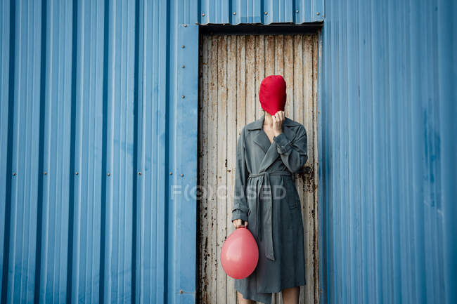 Mujer adulta media cubriendo la cara con sombrero de punto mientras está de pie junto a la puerta corrugada — Stock Photo