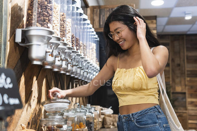 Woman with hand in hair opening glass jar at grocery store — Stock Photo