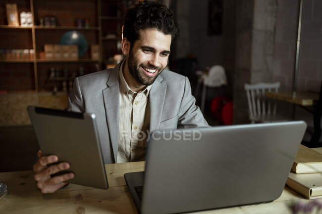 Felice lavoratore freelance maschile con tablet digitale in videochiamata attraverso computer portatile in caffè — Foto stock