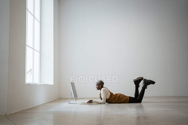 Femme professionnelle utilisant un ordinateur alors qu'elle était allongée sur le devant à la maison — Photo de stock