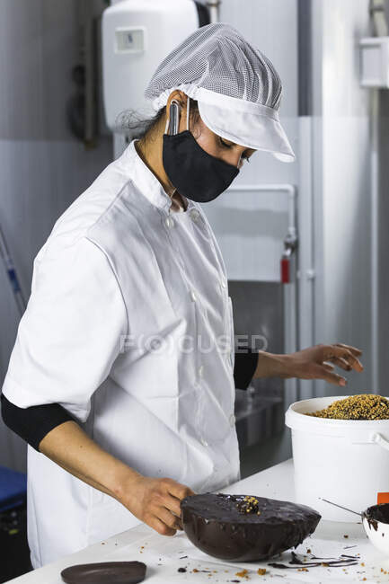 Жіночий пекар з масками для приготування шоколадного десерту на кухні. — стокове фото