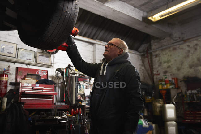 Riparatore senior che esamina i pneumatici nell'industria — Foto stock