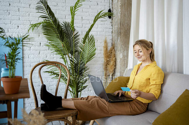 Femme professionnelle utilisant un ordinateur portable détenant crédit tout en étant assis sur le canapé à la maison — Photo de stock