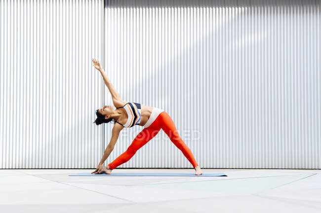 Жінка-спортсменка робить розтягування на тренувальному килимку перед стіною — стокове фото