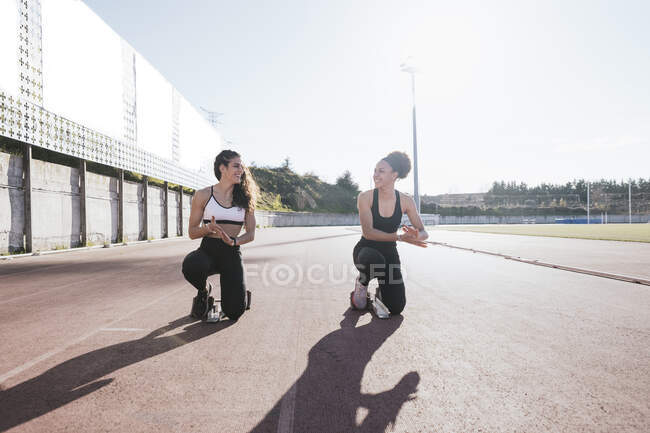 Smiling female friends crouching on training grounds during sunny day — Stock Photo