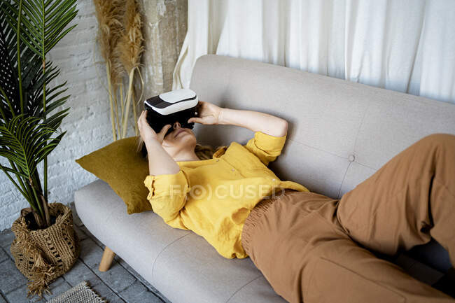 Woman using Virtual reality simulator while lying on sofa at home — Stock Photo