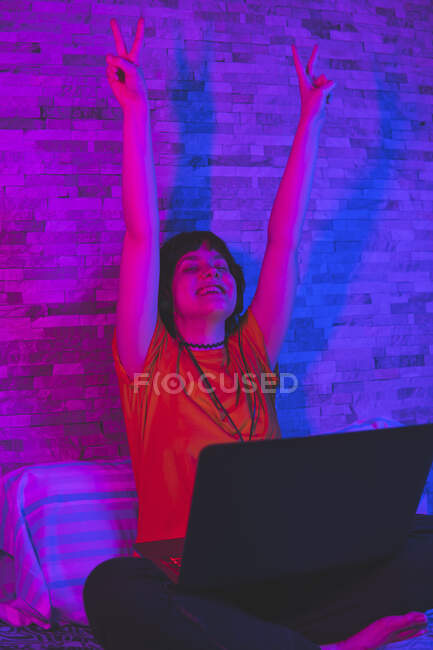 Donna felice mostrando segno di vittoria con le braccia alzate durante la riproduzione di videogiochi sul computer portatile a casa — Foto stock
