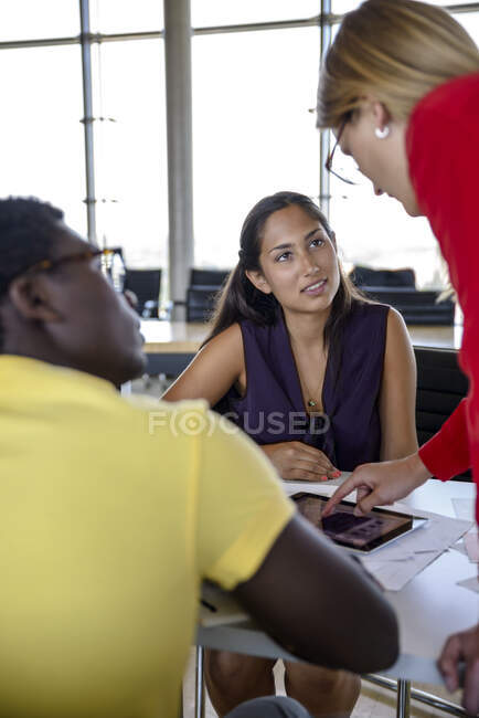 Colegas y colegas mirando a la mujer de negocios explicando a través de tableta digital en la oficina - foto de stock
