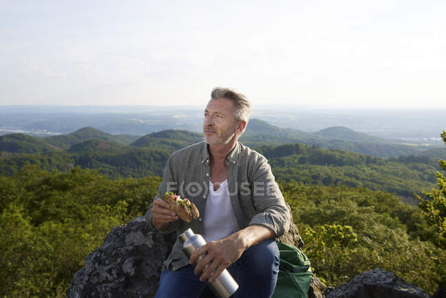 Männlicher Wanderer mit Essen und Flasche auf dem Gipfel des Berges — Stockfoto