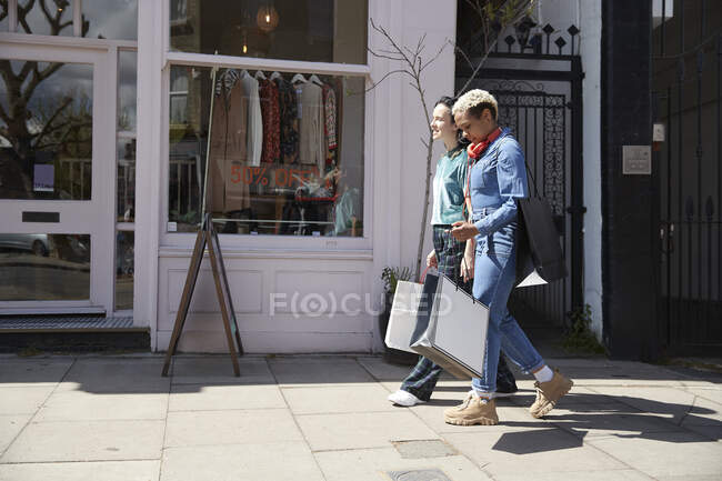 Lesbian couple with shopping bags walking on footpath during sunny day — Stock Photo