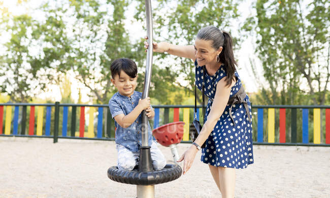 Sorridente nonna sostenere nipote giocare al parco giochi nel parco — Foto stock