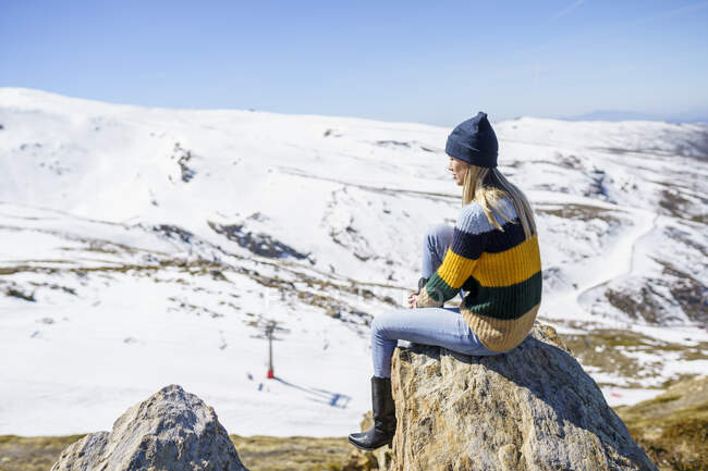 Junge Frau mit Strickmütze sitzt auf Felsen und genießt Urlaub — Stockfoto