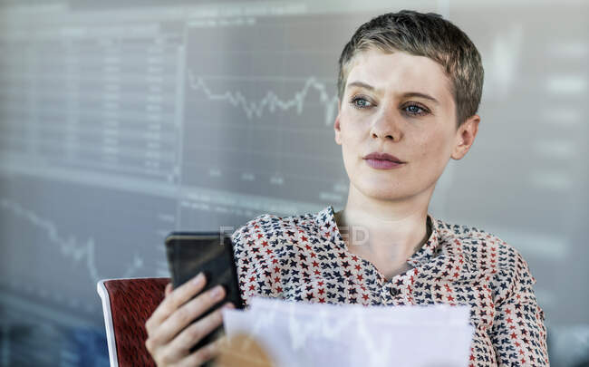 Female professional holding smart phone while looking at graph on digital wall — Stock Photo