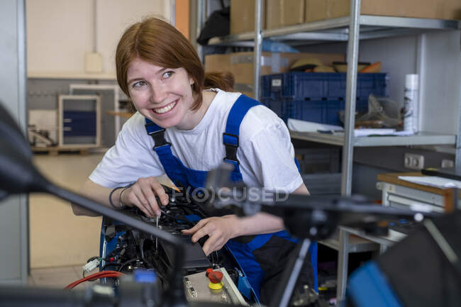 Улыбающаяся женщина-техник смотрит в сторону во время работы в мастерской — стоковое фото