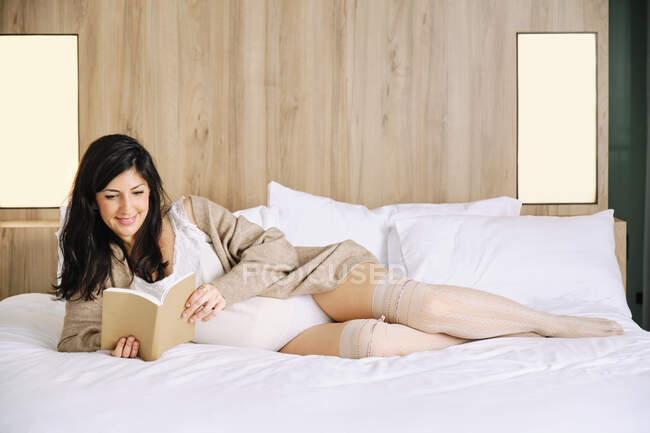 Sourire femme enceinte lecture livre sur le lit à la maison — Photo de stock