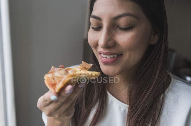 Donna sorridente che tiene la fetta di pizza a casa — Foto stock